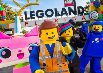 Colorful Legoland Florida entrance with a large Legoland sign and life-sized LEGO mascots posing for the camera in bright costumes.