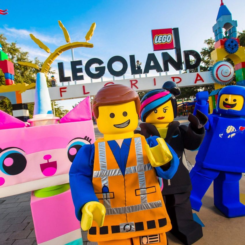 Colorful Legoland Florida entrance with a large Legoland sign and life-sized LEGO mascots posing for the camera in bright costumes.